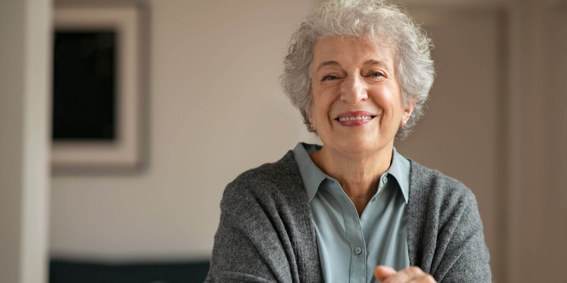 smiling mature woman holding walking stick and sitting on chair at home