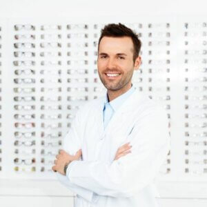 younger male optometrist standing in front of a wall of eyeglasses