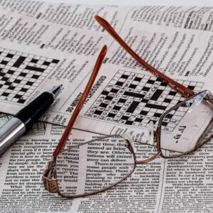 reading glasses lying next to a pen on top of newspaper crossword puzzle