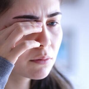 young caucasian women in a sweatshirt rubbing her eye due to having a sore eyelid