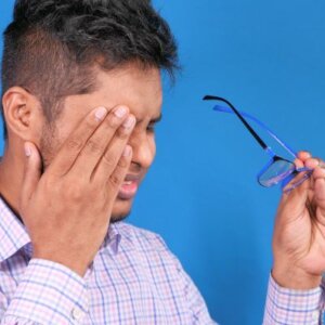 Latino man holding his glasses as he rubs his eye due to swelling from thyroid eye disease