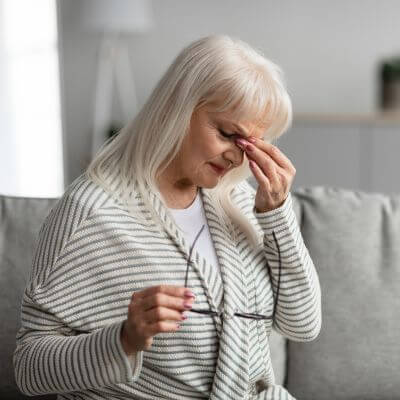 older woman holding her glasses in one hand and rubbing her eyes with the other